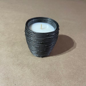 May include: A black candle with a white wax top in a wire container. The wire container has a textured design.