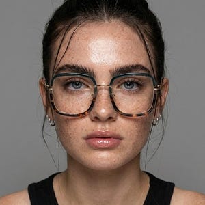 Peut inclure: Lunettes à monture carrée avec un motif écaille de tortue sur les bords inférieurs et les branches. Les montures ont une bordure en métal doré. La personne porte un débardeur noir.