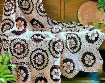 May include: A crocheted throw blanket with a floral pattern in shades of pink and brown. The blanket is draped over a wooden chair.