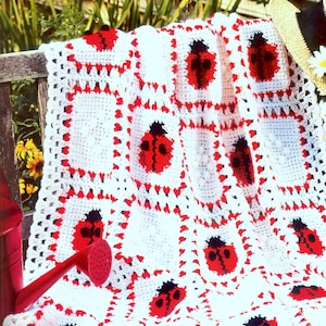 May include: White crochet blanket with red and black ladybug designs. The blanket is made of squares with a red border and a white center. The ladybugs are in the center of each square.
