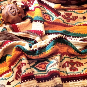 Puede incluir: Una manta de ganchillo colorida con un diseño del suroeste que presenta patrones geométricos y pájaros estilizados. La manta está hecha con una variedad de colores, incluyendo rojo, naranja, amarillo, verde y marrón.