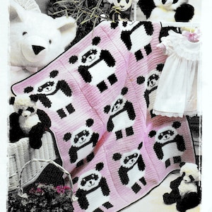 May include: A pink and white crocheted baby blanket with a panda bear design. The blanket is surrounded by stuffed animals, including a white bear, a panda bear, and a small white dress.
