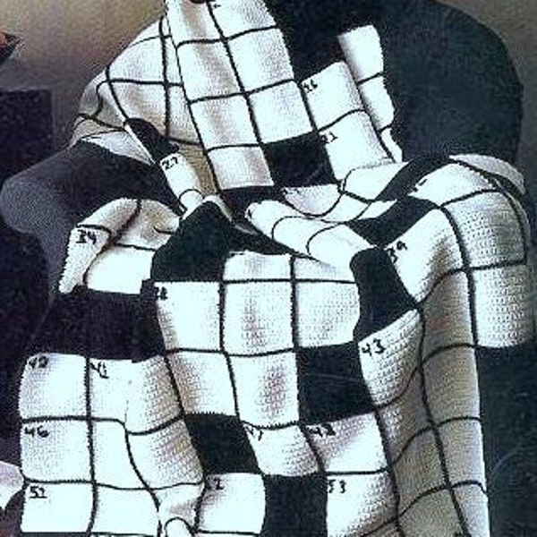 Peut inclure: Une couverture crochetée noire et blanche drapée sur une chaise. La couverture présente un motif quadrillé avec des carrés numérotés, ressemblant à un jeu de mots croisés. La couverture est faite de fil doux et a un aspect fait main et confortable.
