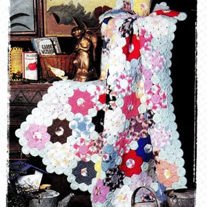 May include: A crocheted blanket with a flower pattern in shades of pink, blue, white, and red. The blanket is folded and draped over a wooden surface with a small figurine and a book titled "Garden Wizard".