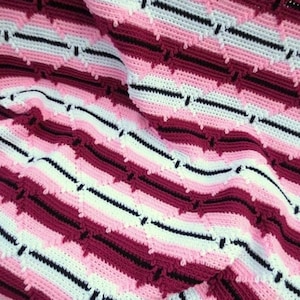 May include: A crocheted blanket with a striped pattern in pink, white, and burgundy.