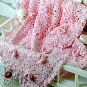 May include: A pink crocheted baby blanket with a delicate floral pattern and a satin ribbon. The blanket is soft and fluffy, perfect for a newborn.