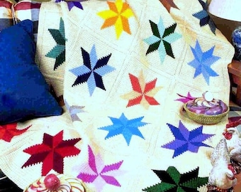 May include: A crocheted blanket with a white background and colorful eight-pointed stars. The blanket is on a couch with a blue pillow and a small table with a decorative bowl.