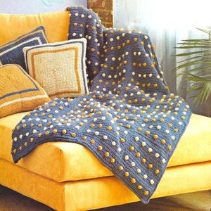 May include: A blue and yellow crocheted throw blanket with a textured dot pattern is draped over a yellow couch with two yellow and white striped pillows and a square yellow and white crocheted pillow.