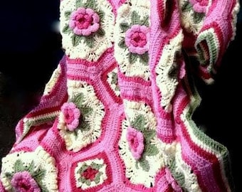May include: A crocheted blanket with a pink and white floral pattern. The blanket is made of soft yarn and has a delicate, feminine feel.
