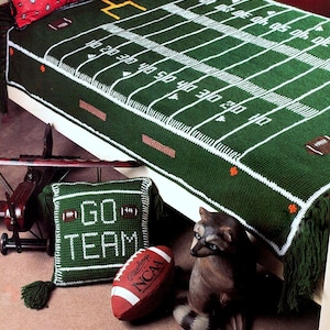 May include: A green crocheted blanket with a football field design. The blanket is on a bed with a pillow that says "GO TEAM" and a football.