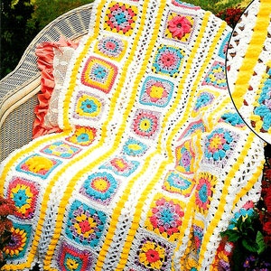 Peut inclure: Une couverture en crochet avec un motif jaune, rose, bleu et blanc. La couverture est composée de carrés avec différents motifs floraux.