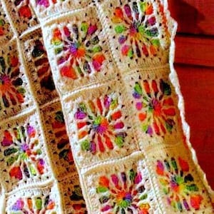 May include: A crocheted blanket with a white background and colorful, multi-colored, circular designs. The blanket is made of yarn and has a scalloped edge.