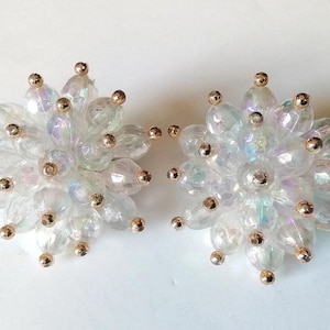 Op de afbeelding: Een paar regenboogkleurige witte oorbellen met gouden accenten. Elke oorbel is een cluster van kleine, ronde kralen.