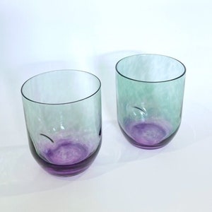 May include: Two clear glass tumblers with a green and purple ombre effect. The glasses are empty and sitting on a white surface.