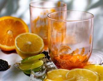 May include: Two clear glasses with orange liquid, surrounded by sliced oranges, lemons, limes, and blackberries. The glasses have a textured, bumpy surface.