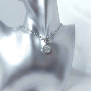 Può includere: Una collana a catena d'argento con chiusura a levetta e un ciondolo rotondo con un design ad albero con cristalli trasparenti.