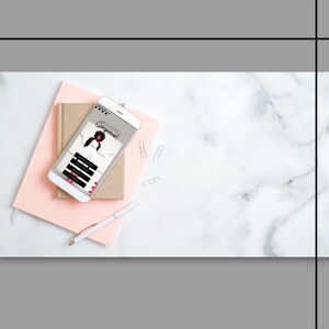 May include: A smartphone displaying a mobile app with the text "Welcome Gorgeous!" on a pink and gold notebook with a white pen on a white marble surface.