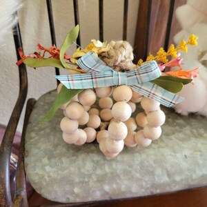 May include: A wooden bead pumpkin with a blue and white plaid bow and fall-colored floral accents.