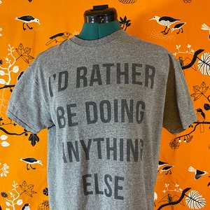 May include: Gray t-shirt with the text "I'd rather be doing anything else" printed in black.