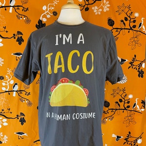 May include: A gray t-shirt with the text "I'm a taco in a human costume" and a cartoon image of a taco.