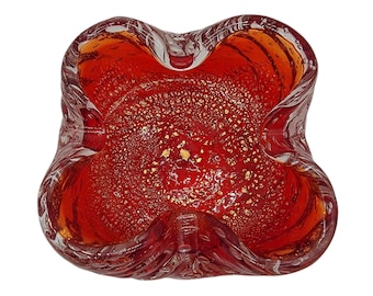 May include: Red glass ashtray with gold flecks. The ashtray has a wavy, organic shape.