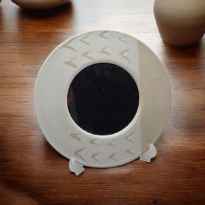 May include: White ceramic mirror with a stand. The mirror has a white background with a pattern of small white birds and a black reflective surface.