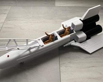 May include: A white toy spaceship with black engine details and two small figures in the cockpit. The spaceship has a long, streamlined body with a detailed wing and tail design. The figures are wearing tan suits.