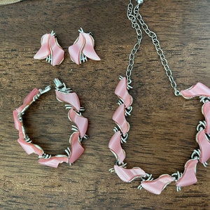 May include: A pink and silver jewelry set with a necklace, bracelet, and earrings. The jewelry features a geometric design with pink stones.