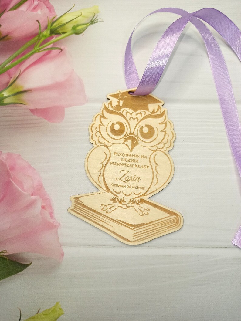 May include: Wooden owl figurine with a graduation cap, holding a book. The owl is decorated with a  "PASOWANIE NA UCZNIA PIERWSZEJ KLASY" inscription and the name "Zosia" with the date "5WRZEDNIA 20.10.2022".