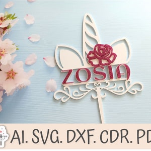 May include: White unicorn cake topper with a pink glitter rose and the name "ZOSIA" written in pink glitter.