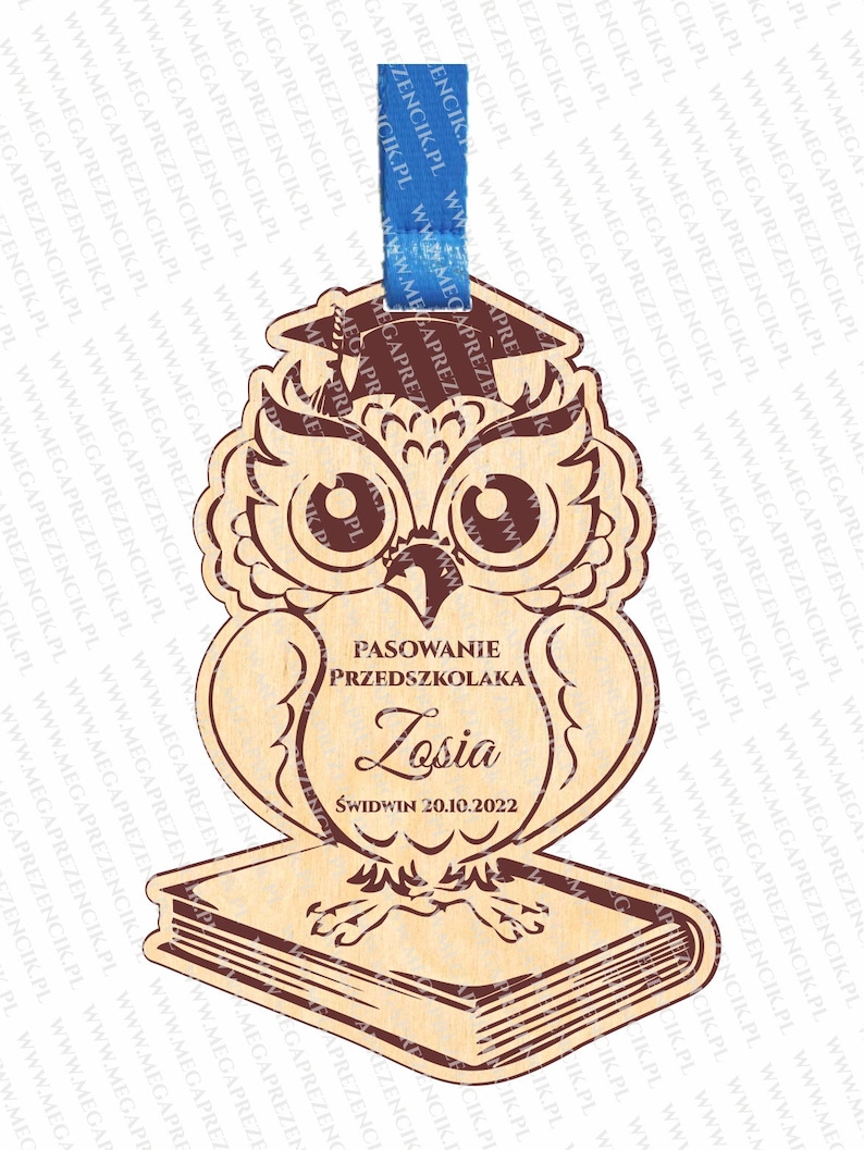 May include: Wooden owl figurine with a graduation cap, holding a book. The owl is brown with red eyes and a brown book. The text on the owl reads "Pasowanie Przedszkolaka Losia Świdwin 20.10.2022".