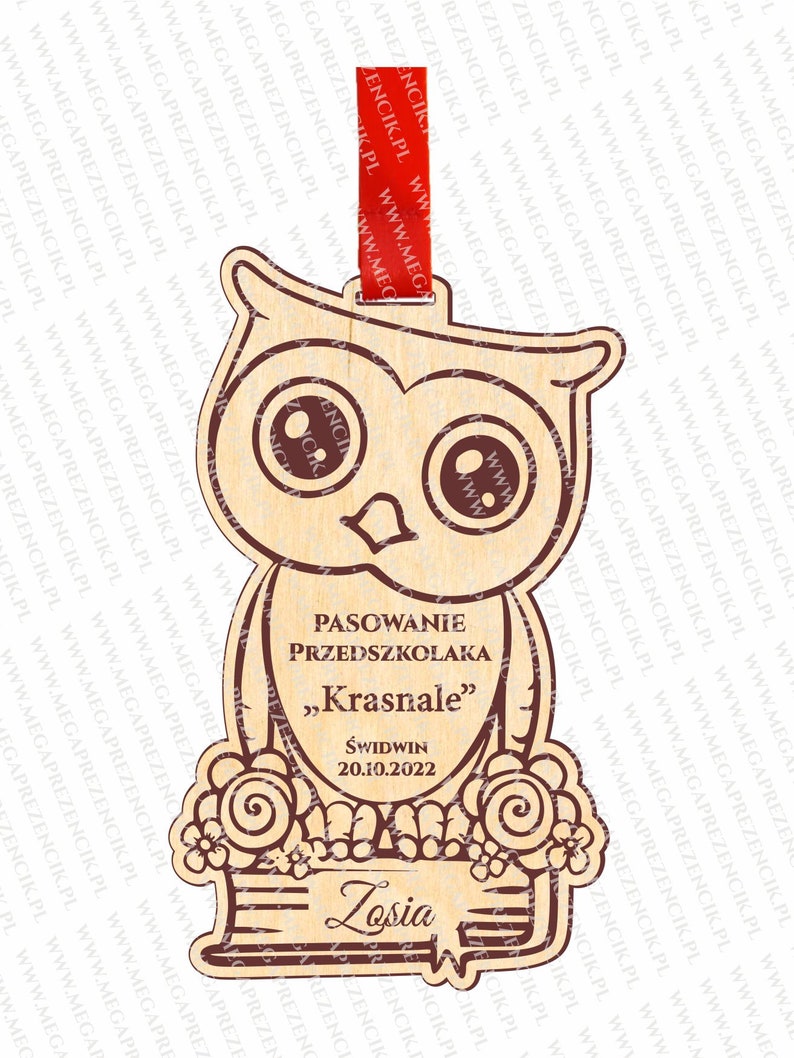 May include: A wooden owl-shaped plaque with a brown outline. The plaque has the text "PASOWANIE PRZEDSZKOLAKA "Krasnale" ŚWIDWIN 20.10.2022" and the name "Zosia" written on it. The plaque is decorated with flowers and a book.