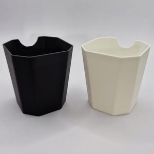 May include: Two geometric planters, one black and one cream, are shown against a white backdrop. Each planter has an angular design with a curved opening at the top. These planters are suitable for indoor or outdoor use, perfect for adding a modern touch.