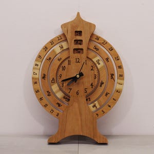 May include: A wooden perpetual calendar and clock with a circular design. The clock face has black hands and Roman numerals. The calendar features a rotating dial with the months of the year and days of the week.