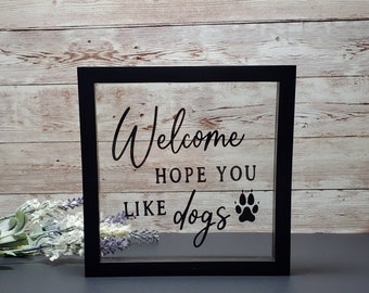 May include: Black framed sign with a clear glass insert. The sign says "Welcome hope you like dogs" with a paw print graphic.