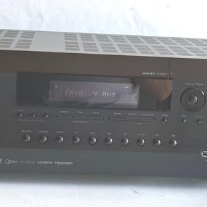 Könnte beinhalten: Schwarzer Integra Audio-Receiver mit digitaler Anzeige von FM 103,9 MHz. Der Receiver hat mehrere Tasten, Knöpfe und Eingangsanschlüsse. Die Oberseite hat ein gitterartiges Design.