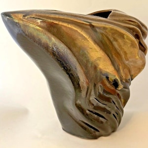 May include: A ceramic vase with an asymmetrical, sculptural form featuring a glossy finish. The surface displays a blend of deep charcoal, metallic bronze, and golden-brown tones with fluid, rippled textures that create a sense of movement.