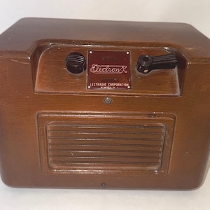 May include: A vintage wooden radio with a dark brown finish. The radio features a rectangular speaker grill, two black knobs, and a rectangular nameplate that reads "ElectronX ELECTRADIO CORPORATION NEWARK N.J."