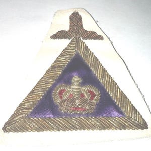 May include: A vintage emblem featuring a purple triangle with a gold-colored border and a gold crown. The emblem is set on a white background and has gold and red accents.