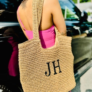 May include: A large, tan, woven tote bag with black handles and the initials "JH" embroidered on the front.