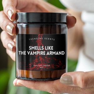 May include: A brown glass candle jar with a black label that reads "Trending Scents" and "Smells Like The Vampire Armand". The label also says "100% Soy Candle 8oz".
