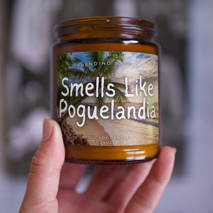 May include: A brown glass candle jar with a white label that says "Trending Scents" and "Smells Like Pogue-landia". The label also says "100% Soy Candle 8 oz".