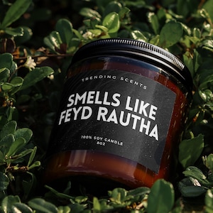 May include: A brown glass candle jar with a black label that reads "Trending Scents, Smells Like Feyd Rautha, 100% Soy Candle, 8 oz". The candle is sitting on a bed of green leaves.