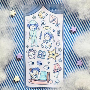 May include: A sticker sheet featuring whimsical illustrations of sleep-themed elements. The designs include cartoon figures in pajamas, a bed, a lamp, a kite, a moon, stars, and an alarm clock. The sticker sheet is on a blue and white striped background with star-shaped embellishments.