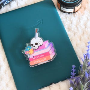 May include: A clear acrylic sticker with a skull, knife, and stack of books. The books are labeled "Mystery" and "Thriller". The sticker has a floral design.