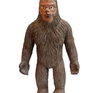 Puede incluir: Figura de juguete Bigfoot marrón con textura de pelaje detallada. La figura tiene una cara marrón con nariz y boca definidas. El juguete está de pie con los brazos a los lados, mostrando un diseño de monstruo clásico.