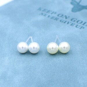 May include: A pair of pearl stud earrings on a blue background. The earrings are made of white pearls and have a silver post.