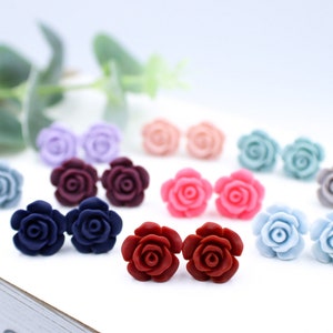 May include: Assortment of 10 pairs of rose-shaped stud earrings in various colours, including light blue, dark blue, burgundy, red, pink, light grey, and lavender.