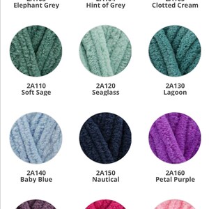 May include: A collection of 12 yarn skeins in various colors, including elephant grey, hint of grey, clotted cream, soft sage, seaglass, lagoon, baby blue, nautical, petal purple, grape, feisty fuchsia, and baby pink. Each skein is labeled with a color name and a product code.