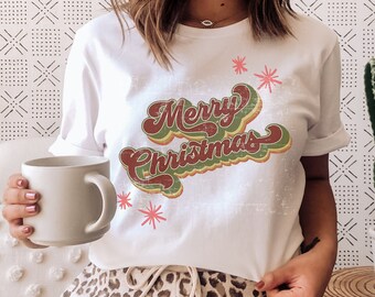 May include: A white t-shirt with a vintage-style "Merry Christmas" graphic in green, red, and yellow. The shirt is distressed and has a faded look. The model is wearing the shirt with leopard print pants.